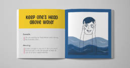 The image shows a mock-up of an opened picture book. An idiom “Keep one’s head above water” is presented on the left page, along with its meaning, an example sentence, and a comical illustration on the right.
