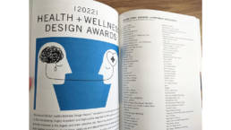 Magazine spread featuring the headline '2022 HEALTH + WELLNESS DESIGN AWARDS' with an illustration of two side-facing human figures. One figure depicts emotional distress with darkness and tears, while the other embodies positivity with a plus-shaped heart in the head.